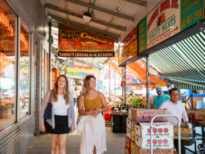 Two women walk past colorful produce stands and market stalls at the lively 9th Street Italian Market.