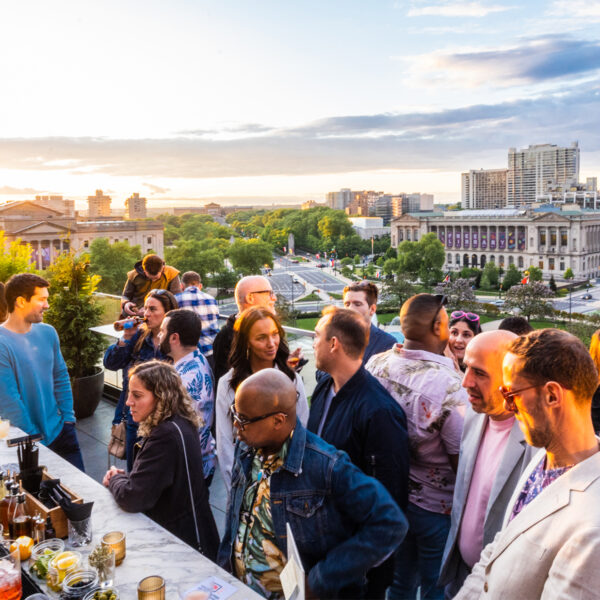 People order drinks at Assembly Rooftop Lounge with a view of the Parkway Central Library in the background as the sun sets.