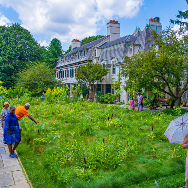 Casually dressed guests explore the lush garden beside the grand historic estate.
