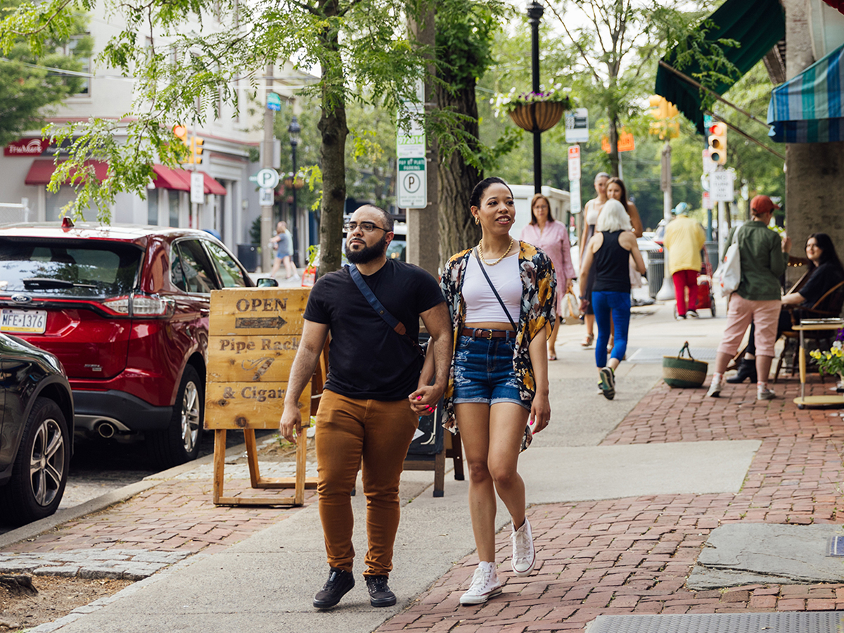 Two people holding hands walks down the concrete and brick sidewalk in the Chestnut Hill neighborhood in Philadelphia.