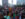 A large, diverse crowd cheers and records a live outdoor performance in front of Philadelphia's City Hall, with flags, raised hands and phones visible throughout the audience.
