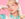 A pop singer poses against a pink background wearing a pastel teal dress, pearl accessories and lace gloves, rest her head on one hand.