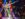 Performers in brightly colored geometric-patterned costumes dance on a circular stage at Fabrika in Philadelphia, illuminated by dramatic spotlights as audience members watch and cheer from surrounding tables.