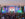 Large crowd gathered in front of a colorful stage at the FIFA World Cup 2026 Fan Festival in Philadelphia, with fans holding up phones and flags as a soccer match plays on a giant central screen.