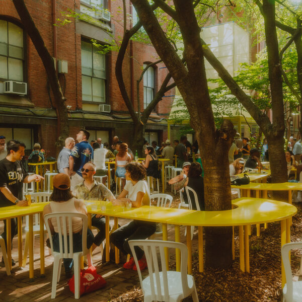 People sit around tree trunks while a yellow table wraps around a tree at Frankie's Summer Club in Philadelphia