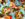 A spread of Laser Wolf menu items set against a teal and white houndstooth pattern. The dishes include fries with ketchup, grilled meats, whole fish with herbs and lemon, pita, an assortment of hummus and other dips. Diners' hands can be seen reaching for food.