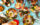 A spread of Laser Wolf menu items set against a teal and white houndstooth pattern. The dishes include fries with ketchup, grilled meats, whole fish with herbs and lemon, pita, an assortment of hummus and other dips. Diners' hands can be seen reaching for food.