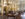 An elegant library decorated with gold light fixtures and wooden furniture displays books on tables and shelves.