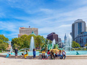 People sit on the edge of a fountain in Logan Square on a beautiful day in Philadelphia
