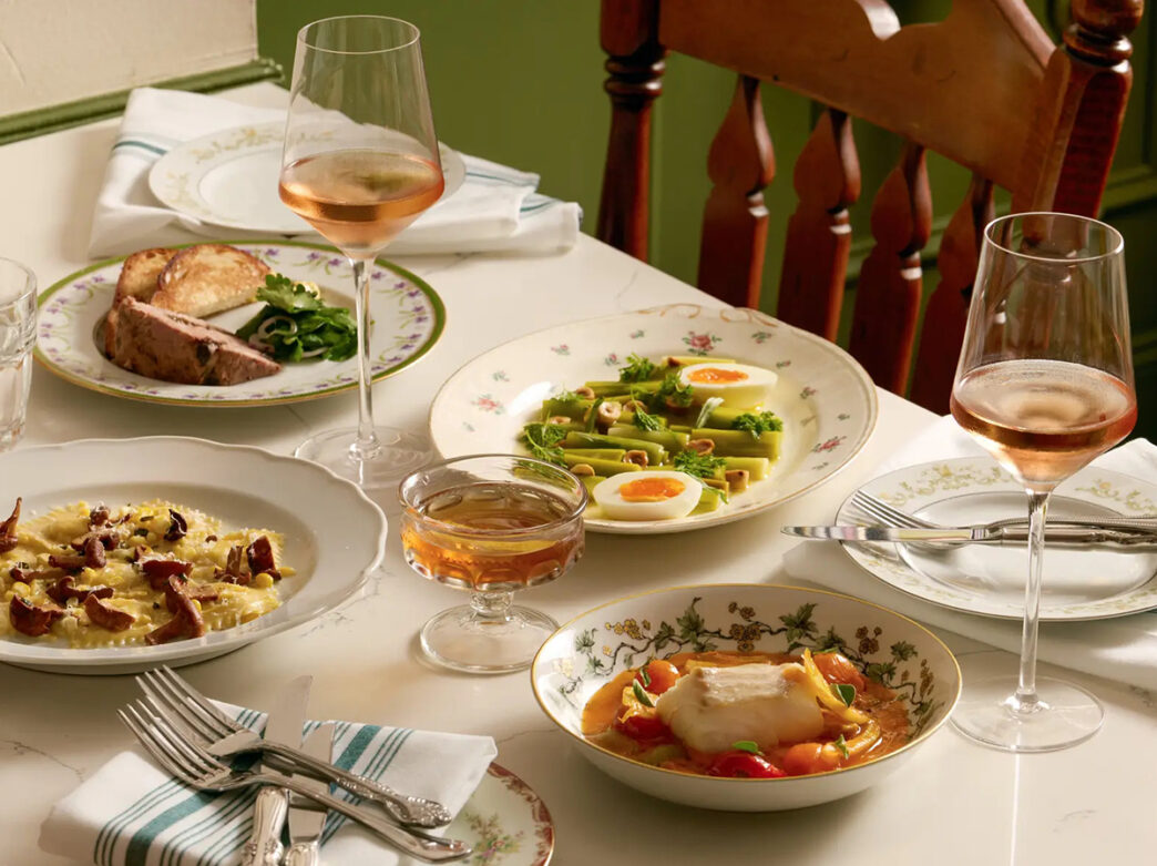A table set with elegant vintage-style plates, glasses of rose and several plated dishes, including pasta, fish and vegetables at Her Place Supper Club.