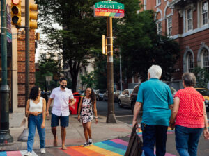 People cross a street in Philadelphia that has a rainbow crosswalk.