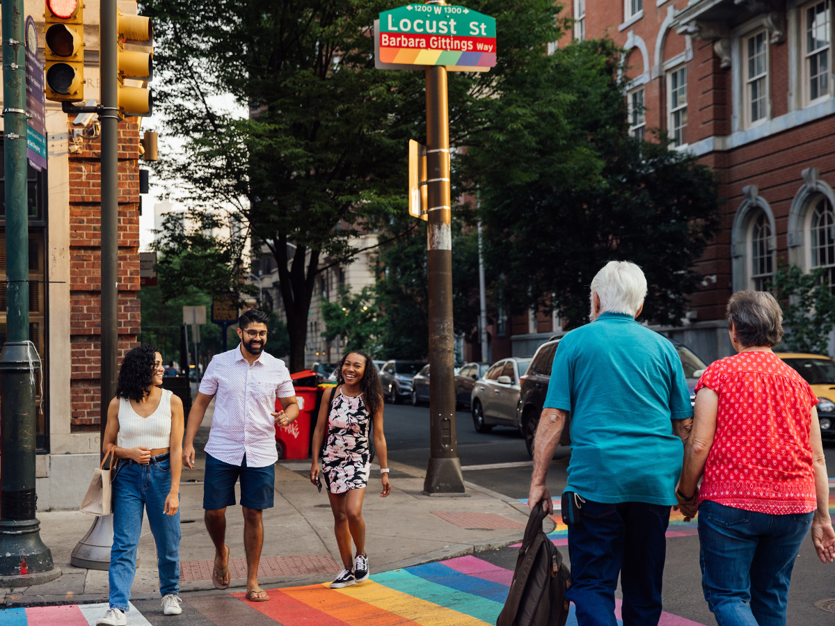 People cross a street in Philadelphia that has a rainbow crosswalk.