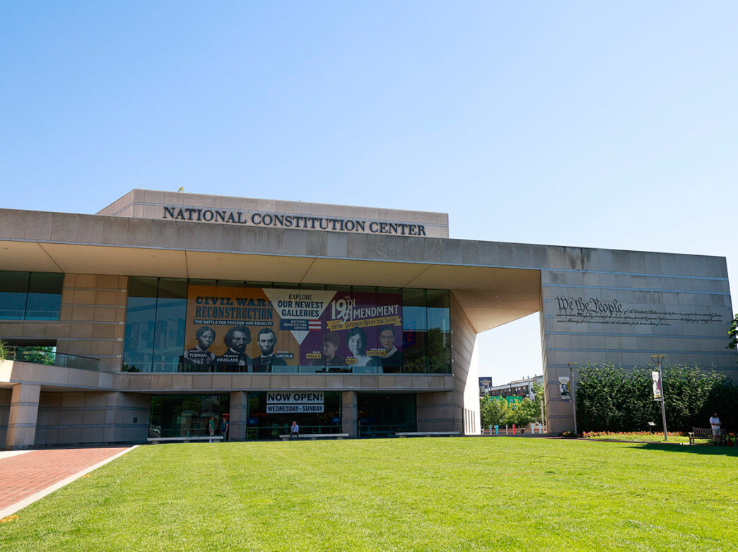 Exterior of National Constitution Center with banner about newest galleries and green grass lawn.