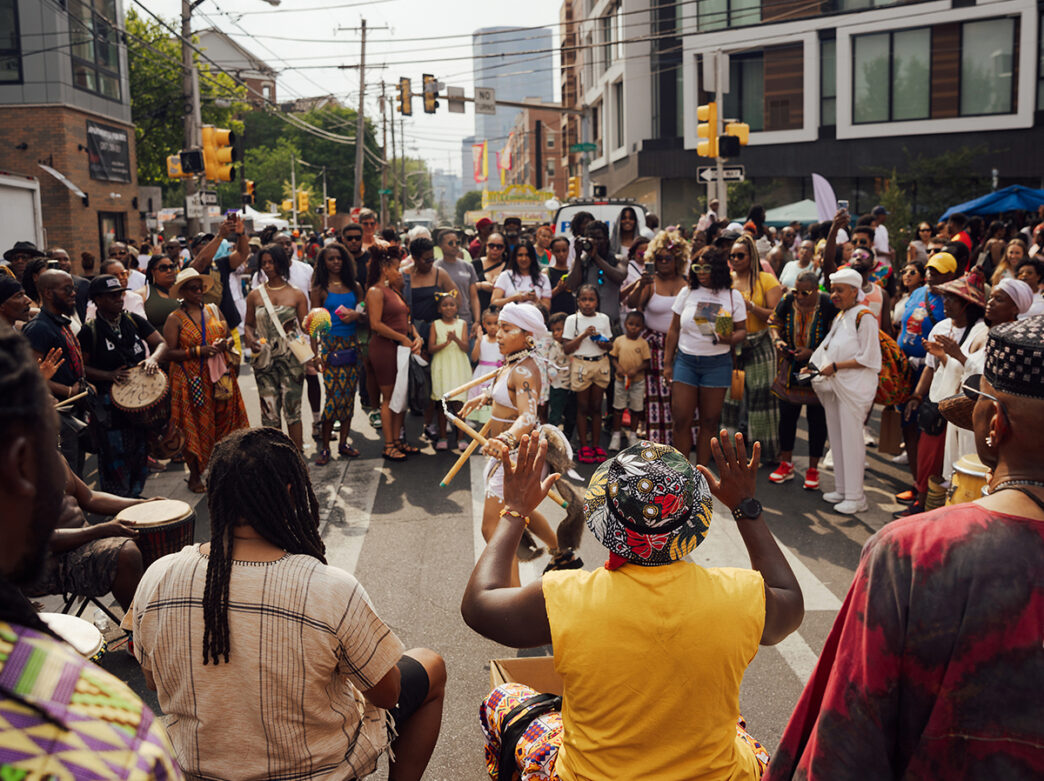 A crowd of onlookers watches a dancer and group of drummers perform at the ODUNDE Street Festival.