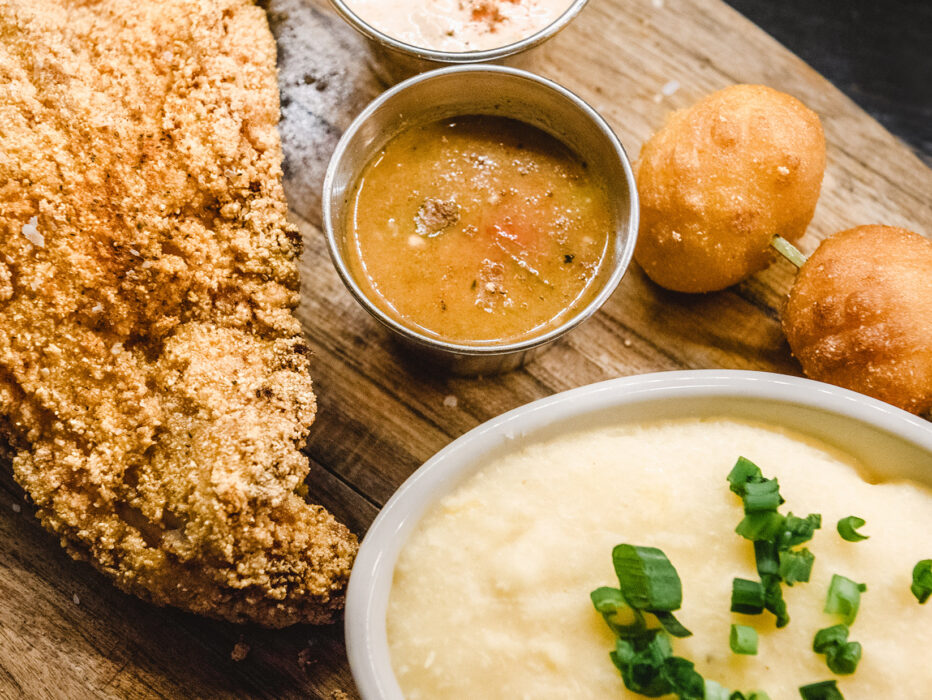A delicious-looking assortment of catfish, mashed potatoes, hush puppies and dipping sauces sit on a wooden plate at SOUTH.