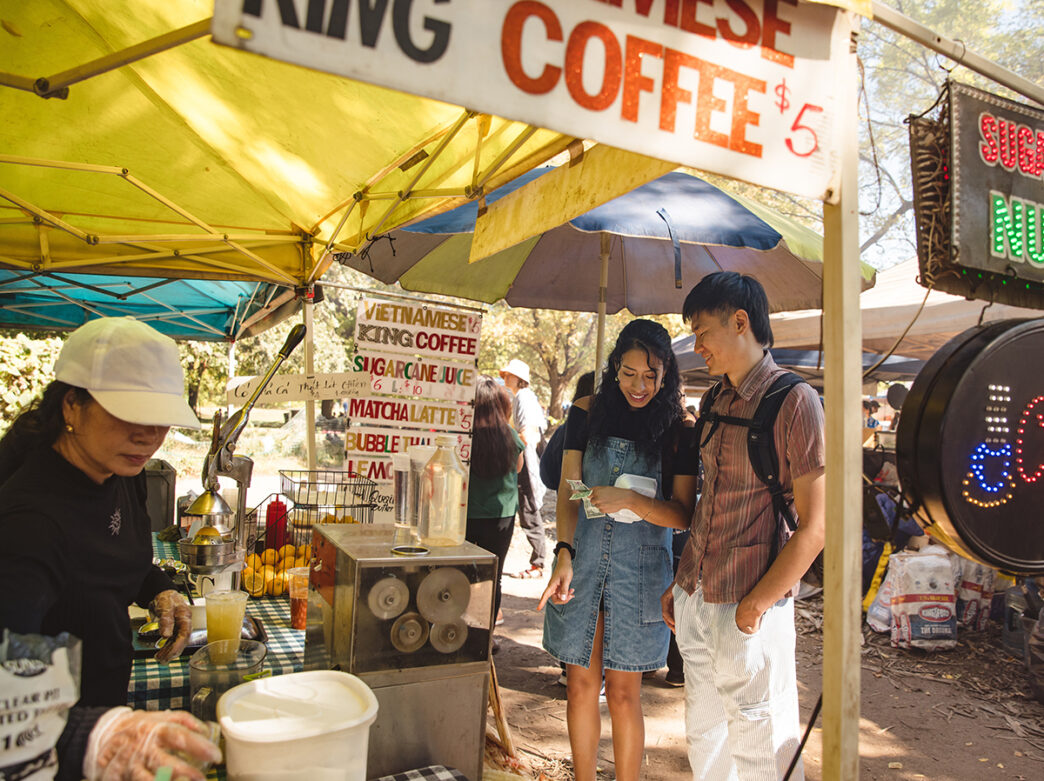 Two people stand next to a food and drink tent at the Southeast Asian Market in Philadelphia. The food vendor sells Vietnamese coffee.