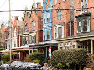 A row of brick Victorian homes with colorful and ornate accents line a residential street in West Philadelphia.