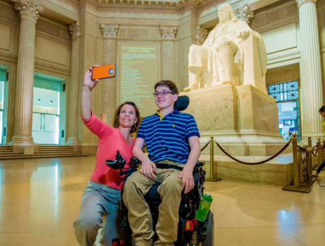 A young visitor using a wheelchair poses for a selfie in accessible The Franklin Institute lobby